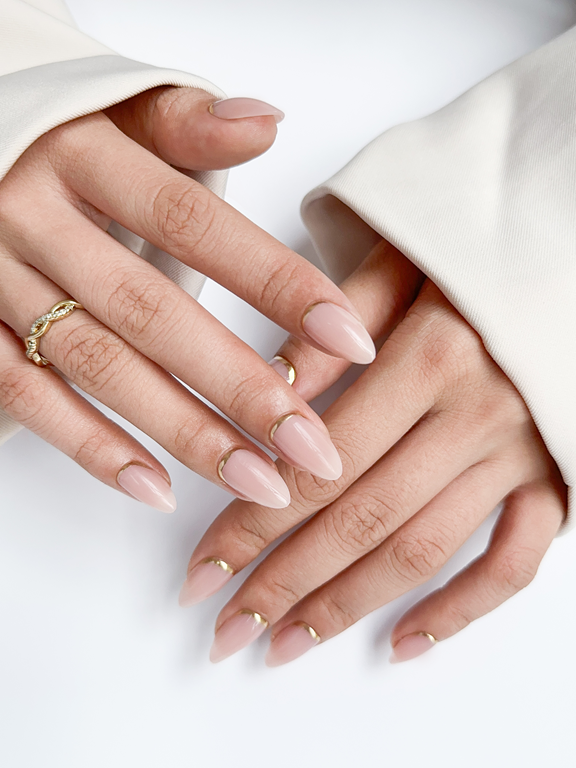 nude almond nails featuring gold reverse French manicure design